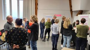 Der Projektraum ist gefüllt mit regen Diskussionen von mehreren Gruppen.